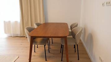 A dining area with a wooden table and four chairs, a window with curtains, and a radiator.