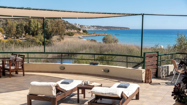 Eine Terrasse mit zwei Holzliegen, einem Tisch und Blick auf das Meer und die Hügel.