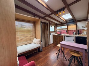A compact kitchen with a sink, stove, and a small dining area with stools. - Casa Bohèm - Cosy beach studio for two (Zandvoort)