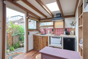 A compact kitchen with wooden beams, a dishwasher, a coffee machine, and a view of a garden.