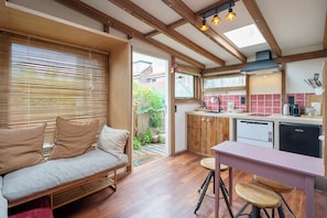 A cozy kitchen with wooden beams, a dining area with stools, and a sofa with cushions. - Casa Bohèm - Cosy beach studio for two (Zandvoort)