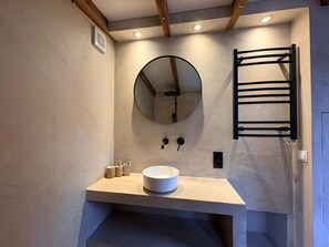A bathroom with a round mirror, a towel rack, and a sink with a beige countertop. - Casa Bohèm - Cosy beach studio for two (Zandvoort)