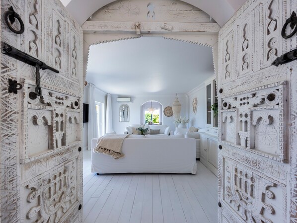 Ein Zimmer mit einem großen Bett, weißen Wänden und aufwendigen Schnitzereien.