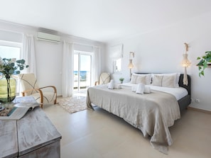 Ein Schlafzimmer mit einem Bett, einem Sessel, einem Tisch mit einer Zeitschrift und Meerblick durch eine Schiebetür.