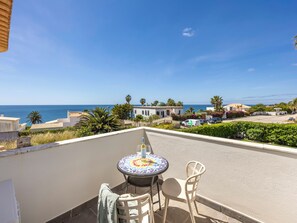 A balcony with a table and chairs overlooking a coastal view.