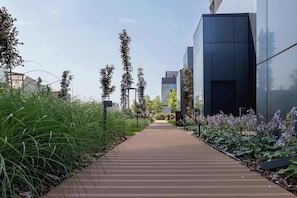 Ein Weg führt zu einem modernen Gebäude mit Glasfassade, umgeben von Grünpflanzen und hoher Vegetation.