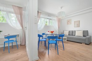 Moderni olohuone, jossa on harmaa sohva, siniset tuolit, ruokapöytä tuoleineen ja läpikuultavat verhot.