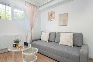 A living room with a grey sofa, two cushions, a small table with a plant, a candle, and two cups. - Bright Apartment in the City Centre | Family City Break (Łódź)