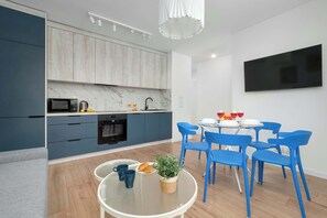 A modern kitchen with grey cabinets, a microwave, and a kettle. There's a dining area with a round table and blue chairs. - Bright Apartment in the City Centre | Family City Break (Łódź)