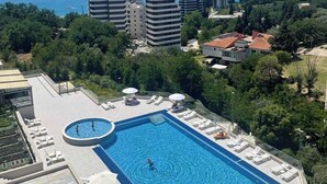 Une piscine sur le toit, agrémentée de chaises longues et de parasols, entourée de verdure et de bâtiments, et offrant une vue sur une étendue d’eau.