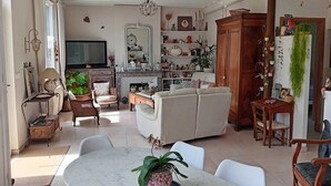 A living room with a sofa, chairs, a dining table, a TV, and various decorative items.