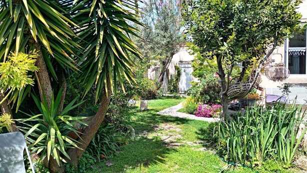 A garden pathway leading to a building with a white facade and a red-tiled roof.