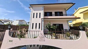 Una casa de dos pisos con balcón, entrada con reja y cielo despejado.