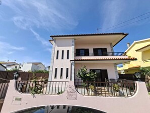 A two-story house with a balcony, a gated entrance, and a clear sky. - Constança House 10 min. from Fonte da Telha (Corroios)
