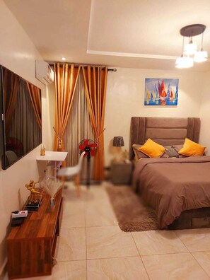Un dormitorio con cama, escritorio, silla, ventilador, lámpara y un cuadro en la pared.