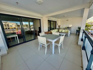En balkon med spisebord og stole, en sofa med puder samt et tekøkken.