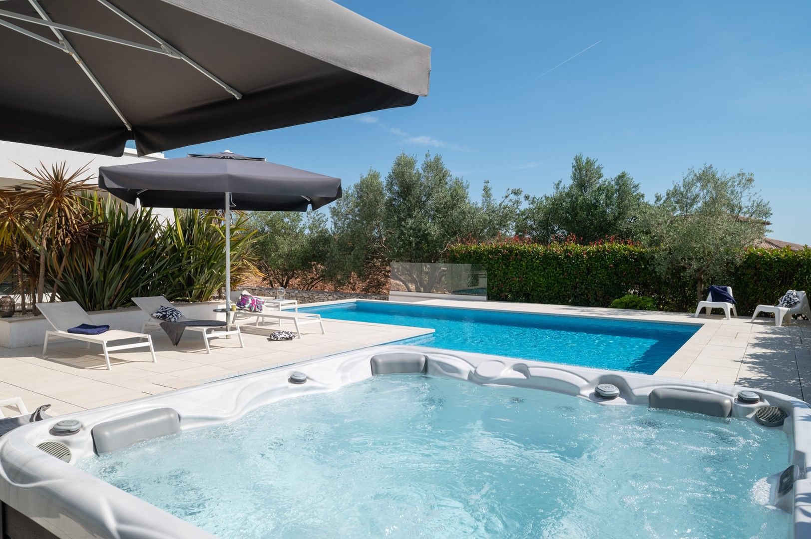 Une piscine avec un jacuzzi, des chaises longues et des parasols.