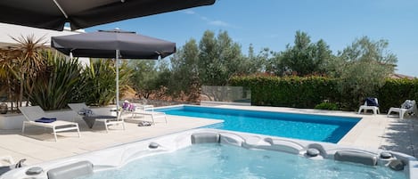 A swimming pool with a hot tub, lounge chairs, and umbrellas.