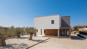 Une maison moderne à deux étages, dotée d’un toit plat, d’une petite fenêtre et d’une allée pavée.