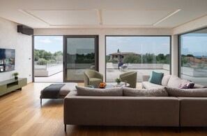 Un salon moderne avec un grand canapé, une table basse et un téléviseur. Une porte-fenêtre coulissante donne accès à un espace patio extérieur.