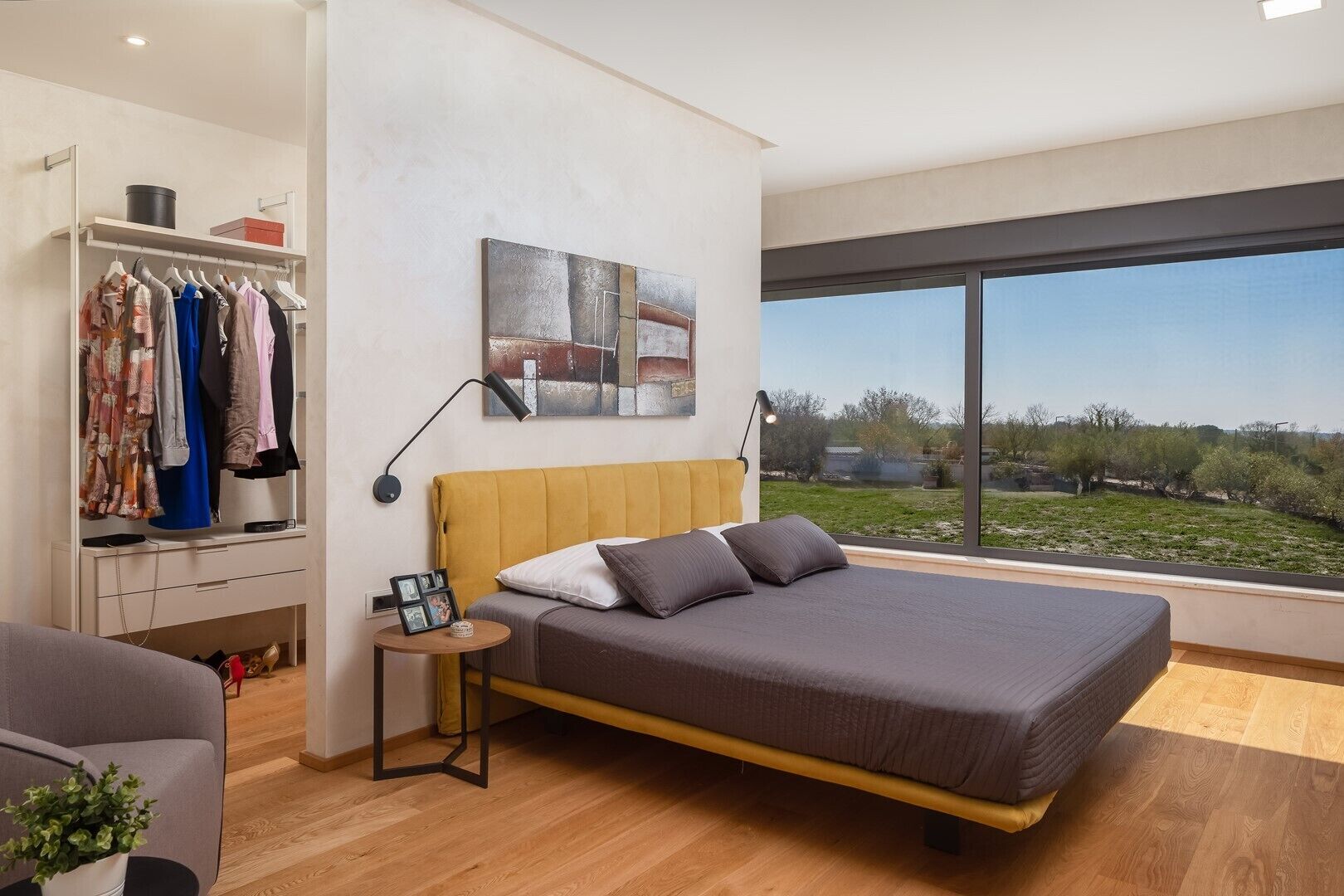 Une chambre moderne avec un grand lit, une armoire, une table de chevet avec une lampe et une vue sur l’extérieur.