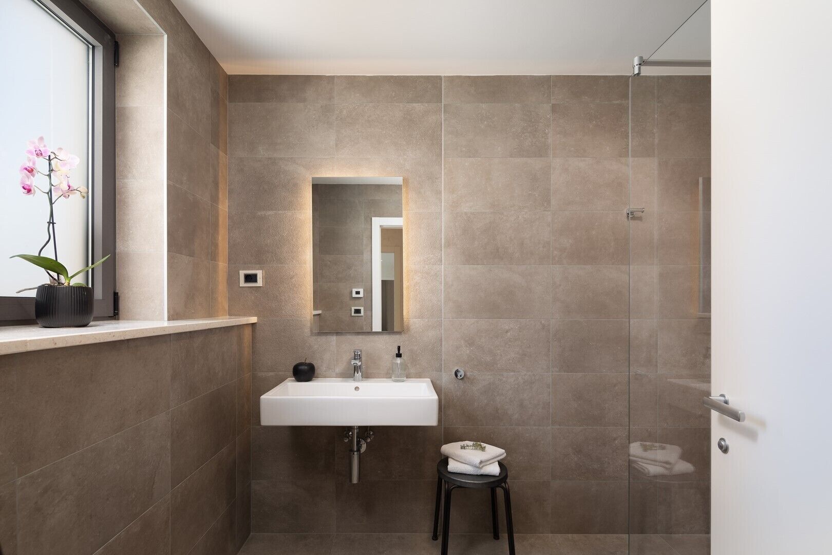 Un baño moderno con un espejo grande, un lavamanos y una ducha.