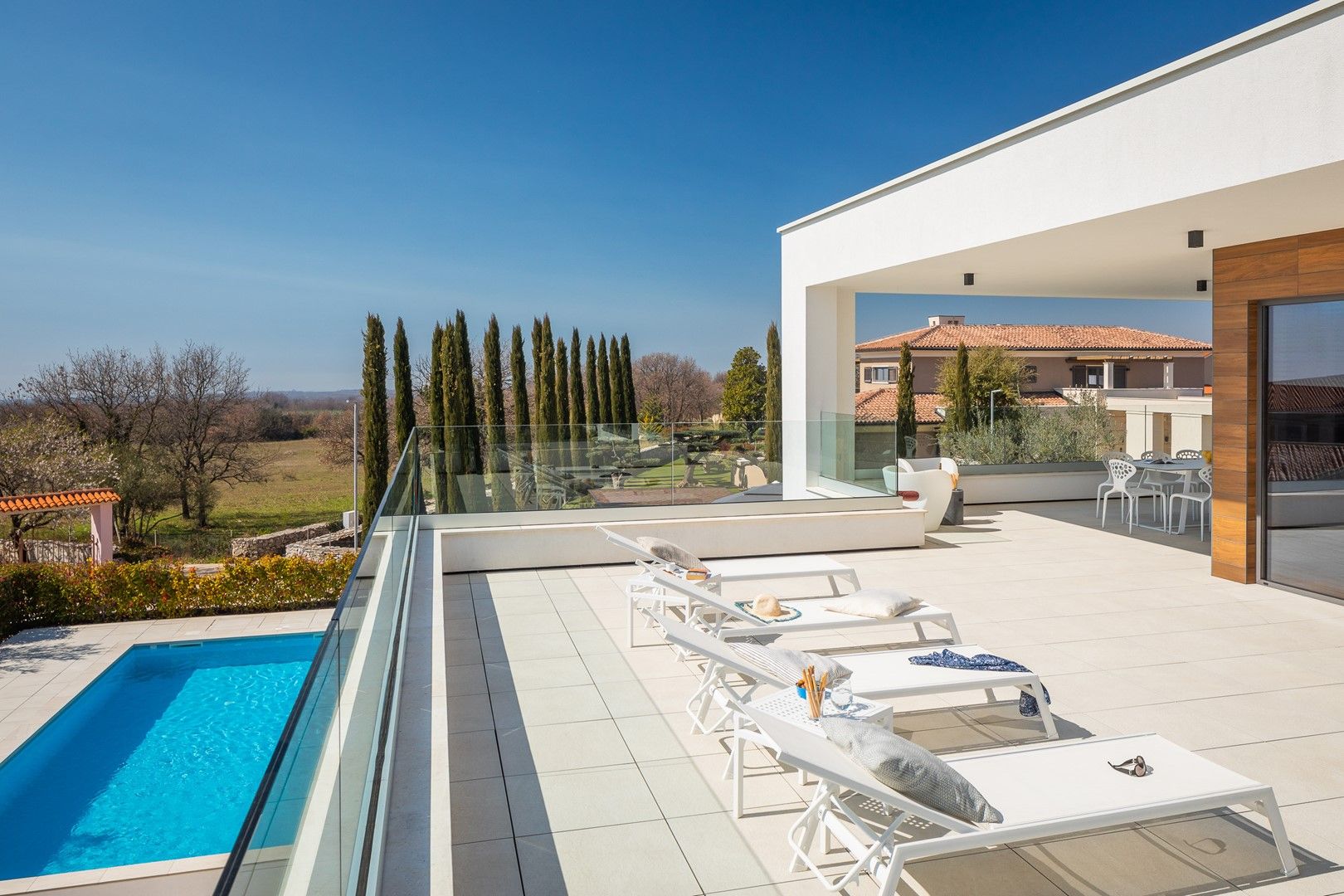 Un espace piscine extérieur moderne, doté de chaises longues et d’une balustrade en verre donnant sur un jardin aménagé.