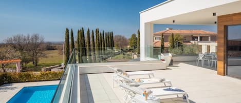 A modern outdoor pool area with lounge chairs and a glass balustrade overlooking a landscaped garden.