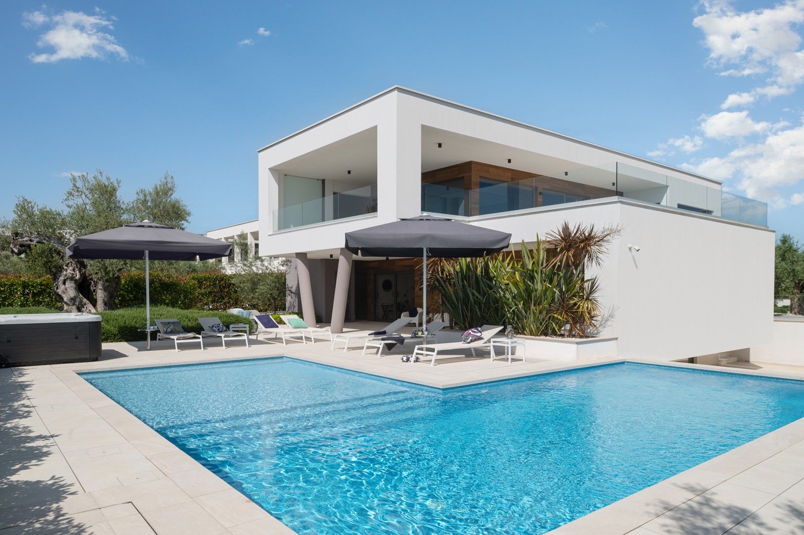 Una casa moderna de dos pisos amb piscina, seients a l'aire lliure i banyera d'hidromassatge.