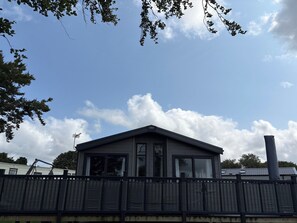 A single-story house with a dark roof, large windows, and a visible chimney. - Harrogate Lodge - Sleeps4- South Facing Decking (Holsworthy)