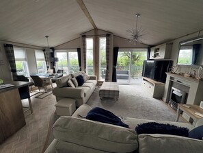 A spacious living area with a sofa, a television, a fireplace, and a balcony with a view. - Harrogate Lodge - Sleeps4- South Facing Decking (Holsworthy)