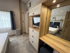 A bedroom with a bed, a TV, a dresser, a mirror, and a window with curtains. - Luxury Harrogate Lodge South Facing Decking (Holsworthy)