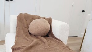 Un lit avec une couverture marron et un oreiller rond, une tête de lit blanche et des murs blancs.