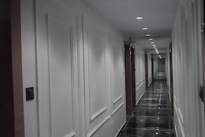 Un pasillo largo y estrecho con paredes blancas y un suelo negro brillante, que conduce a una puerta al final.