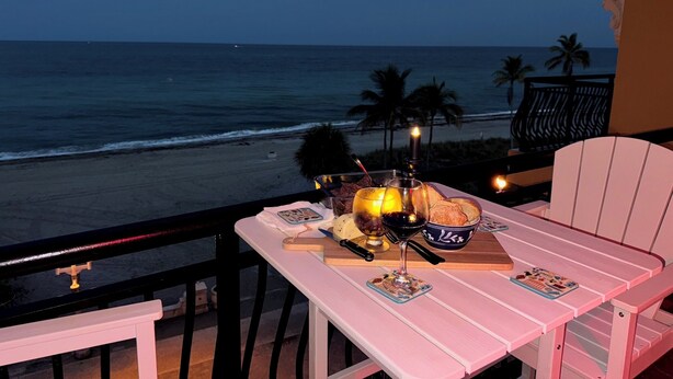 Un balcone con tavolo apparecchiato per cena, vista su una spiaggia con palme e l'oceano.