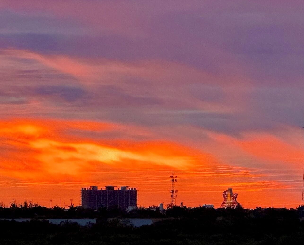 Un coucher de soleil avec des bâtiments se détachant en silhouette sur le ciel.