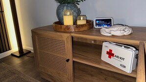 Un comodino in legno con una piccola pianta in vaso, candele, un dispositivo digitale e un kit di pronto soccorso.