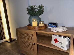 Ein Nachttisch aus Holz mit einem kleinen Topfpflanzen, Kerzen, einem digitalen Gerät und einer Erste-Hilfe-Ausrüstung.