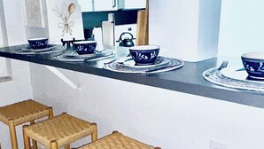 Una cucina con un piano di lavoro, tre sgabelli intrecciati e un bollitore.