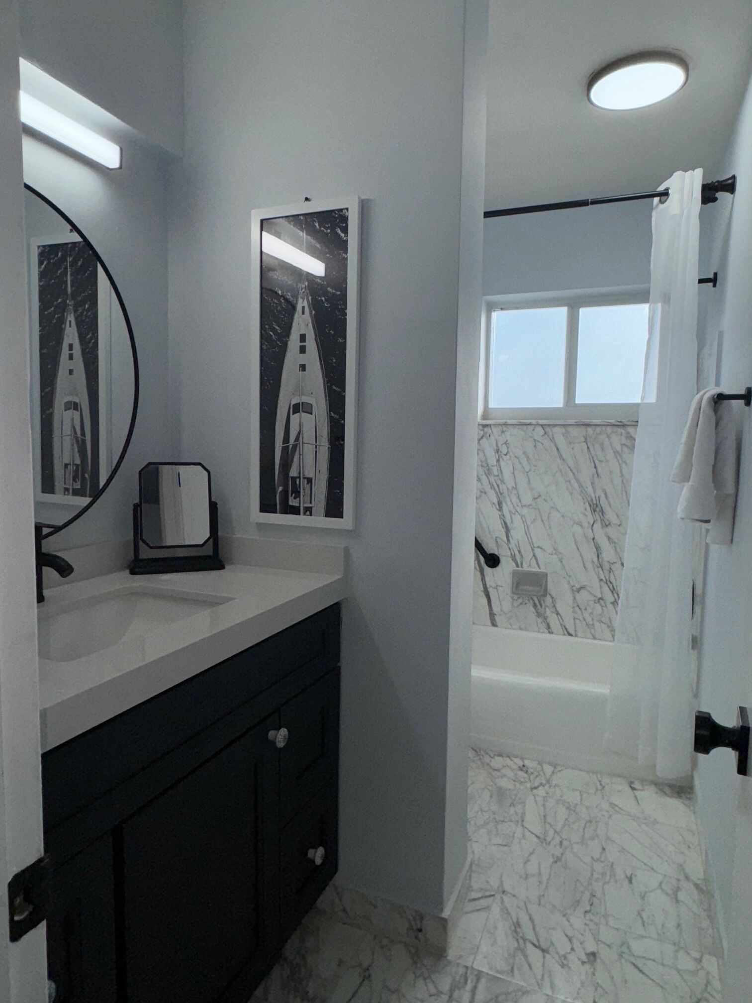 A bathroom with a white sink, a mirror, two framed pictures, a bathtub, and a shower curtain.