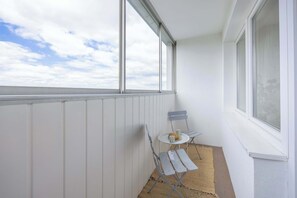 Ein Balkon mit Blick auf den Himmel, ein Tischchen mit einem Stuhl und ein Fenster.