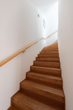 Eine Holztreppe mit Handlauf, weißen Wänden und einer Lampe oben.