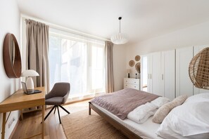 Ein Schlafzimmer mit Bett, Schreibtisch, Stuhl, Kleiderschrank und einem großen Fenster.
