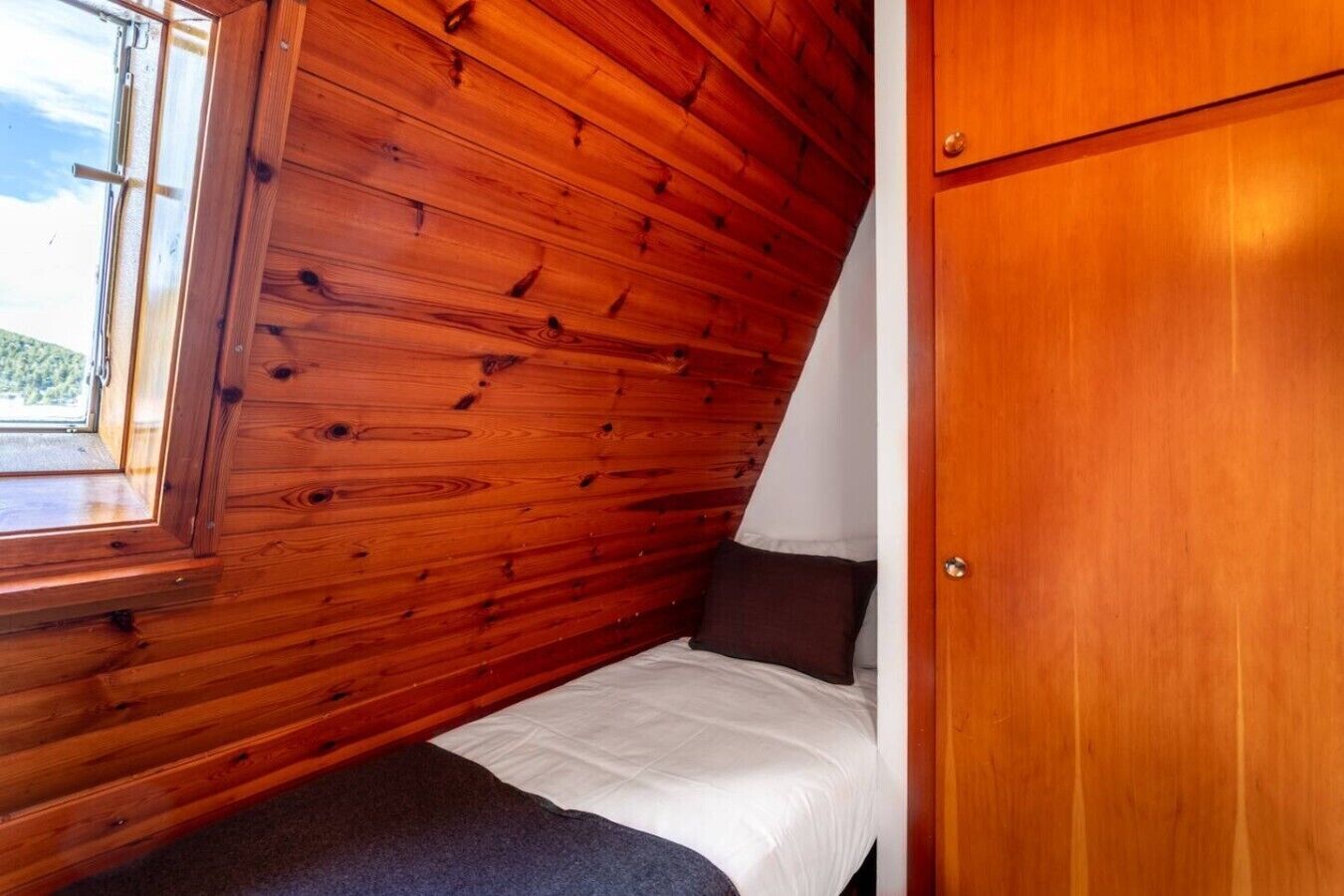 Een kamer met houten wanden, een raam, een bed en een kledingkast.
