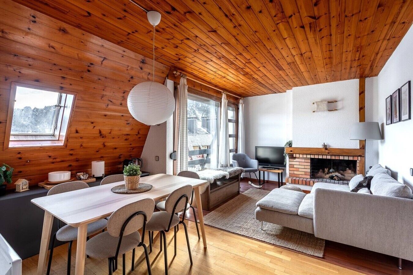 Een gezellig chaletinterieur met houten plafond, een eethoek, een bank, een open haard en een televisie.