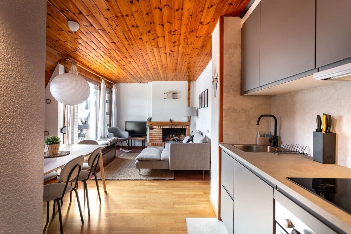 Een moderne keuken met een houten plafond, een eethoek met stoelen en een tafel, en een woonkamer met een bank en open haard.