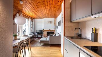 Een moderne keuken met een houten plafond, een eethoek met stoelen en een tafel, en een woonkamer met een bank en open haard.