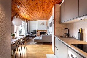 Une cuisine moderne avec un plafond en bois, un coin repas avec des chaises et une table, et un salon avec un canapé et une cheminée.