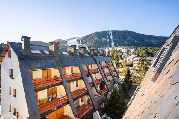 Un immeuble à plusieurs étages, doté d’un toit en pente, de balcons et offrant une vue sur une montagne et une cascade.