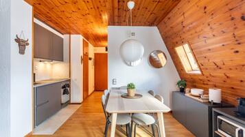 Een moderne keuken met houten plafond, een eethoek met een witte tafel, en een kleine eettafel met stoelen.